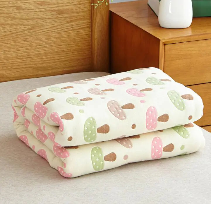White folded blanket with pastel mushroom pattern in pink and green next to wooden dresser.