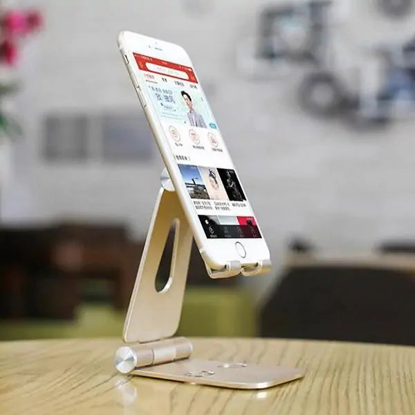 White smartphone in gold folding stand displaying app interface on wooden table