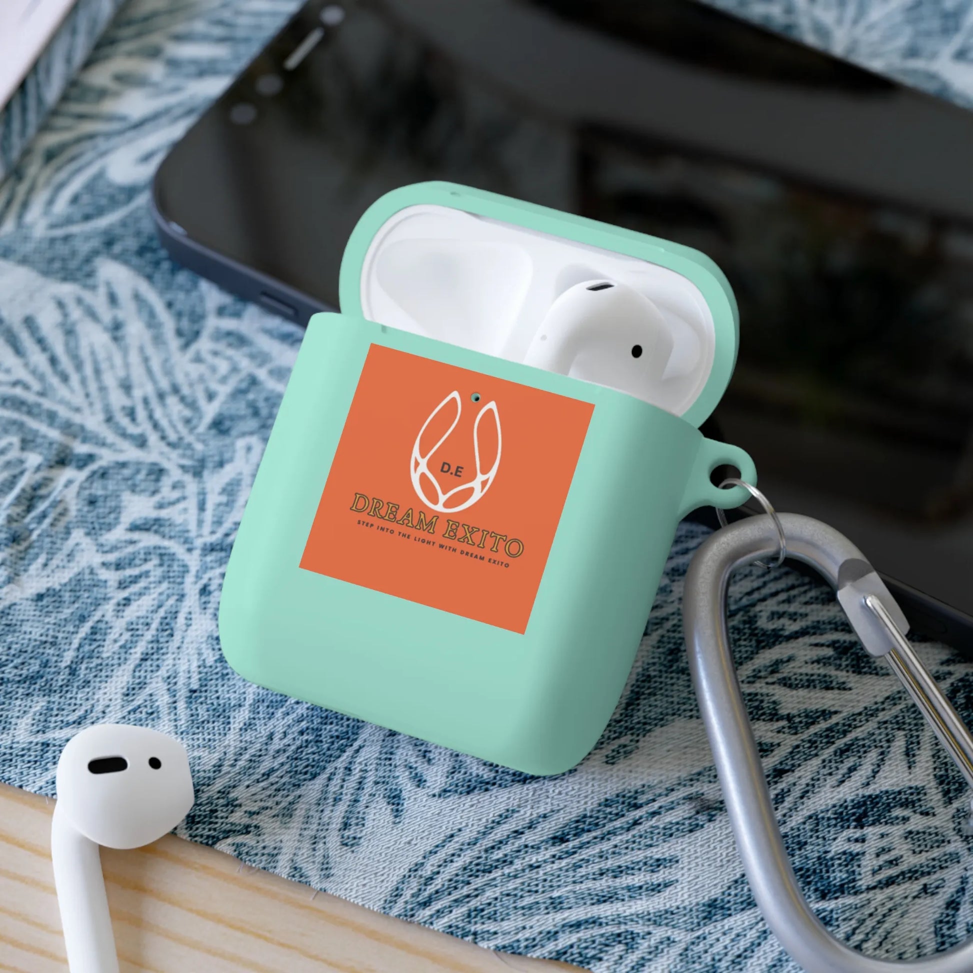 Wireless earbuds in a mint green case with an orange label, on a blue and white patterned surface.