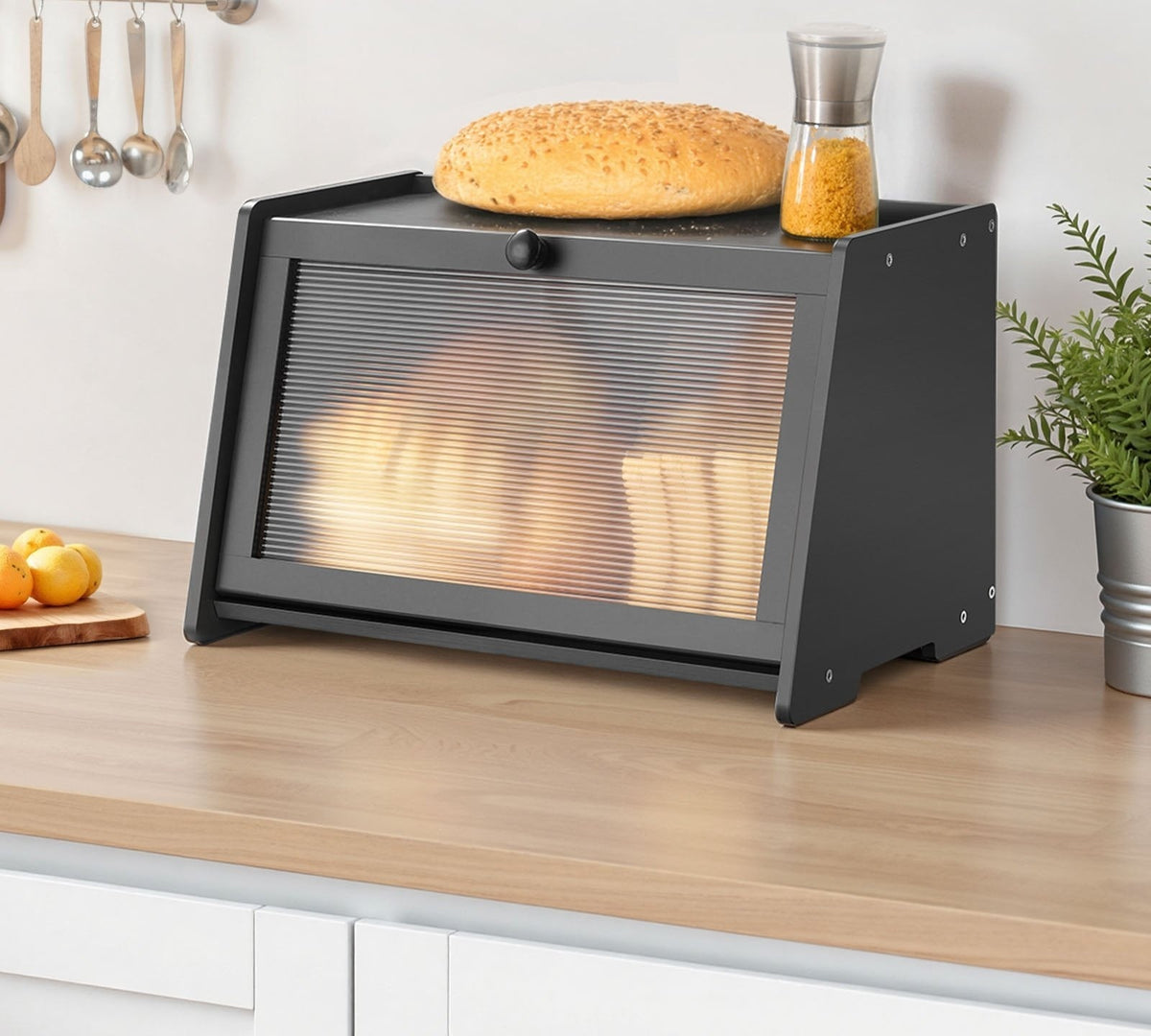Black bread box with a ribbed panel door on a kitchen counter, a round loaf on top