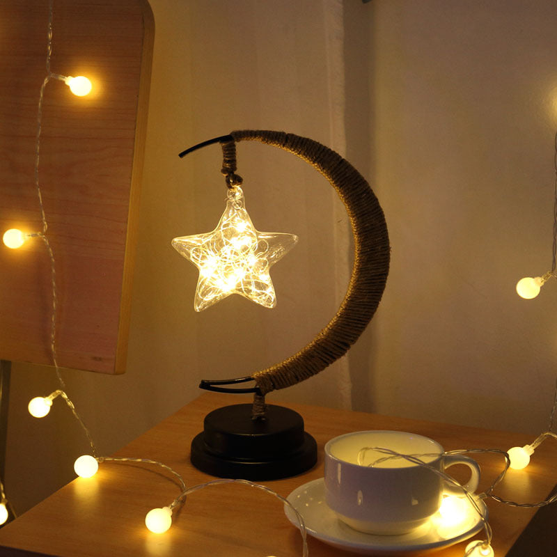 Moon-shaped glass night light with hanging star emitting warm glow on wooden table