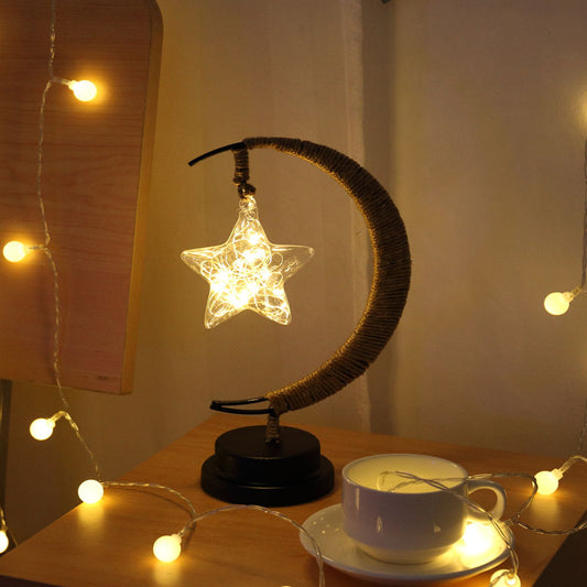 Moon-shaped glass night light with hanging star emitting warm glow on wooden table