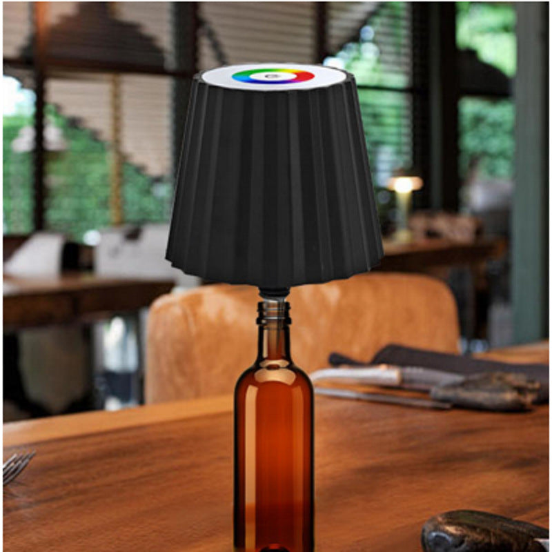 Black wine bottle cap desk lamp with RGB lighting displayed on a brown bottle on wooden table